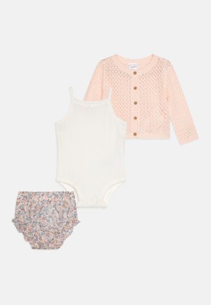Ensemble pour bébé en trois pièces : cardigan en tricot rose clair, débardeur en mailles blanches et culottes volantées à imprimé floral dans des couleurs pastel. Boutons sur le cardigan.