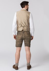 Gilet en satin beige avec une sangle dans le dos, associé à un short en cuir marron au fini texturé, porté avec des chaussures marron et des chaussettes grises.