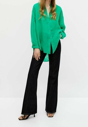 Camicia verde con bottoni e maniche lunghe; abbinata a jeans neri a zampa d'elefante. La camicia è realizzata in un materiale leggero con una texture liscia.