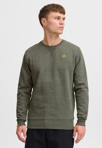 Olive green sweatshirt with long sleeves, ribbed cuffs, a crew neck, and a yellow logo accent on the chest. Made from textured fabric.