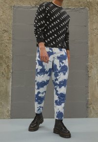 Sudadera negra con patrón de texto blanco, combinada con jeans azul tintado con efecto tie-dye y textura. Modelo con botas negras de cordones y suela gruesa.