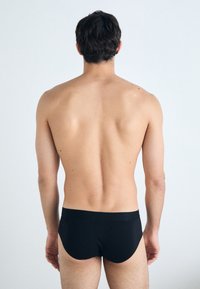 Caleçons noirs pour hommes, en tissu lisse, avec une taille basse, des coutures minimales et une coupe ajustée. Modèle montré de dos.