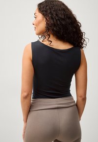 Top nero senza maniche realizzato in tessuto liscio, con scollatura rotonda e un design aderente, abbinato a leggings beige a vita alta.