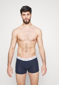 Boxer-briefs bleu marine avec une ceinture blanche arborant le logo "TOMMY HILFIGER". Fabriqués en tissu lisse et extensible. Le modèle montre l'ajustement.