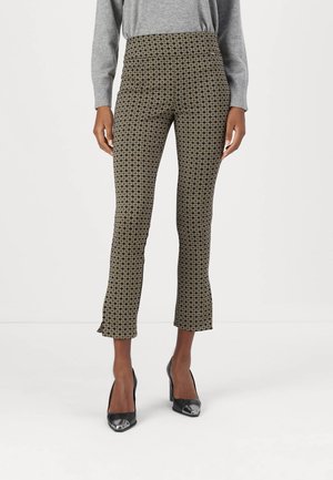 Schwarz-gold gemusterte Hose mit taillierter Passform, hoher Taille und gekürztem, ausgestelltem Saum. Kombiniert mit schwarzen Pumps.