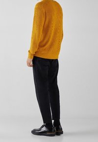 Gelber Strickpullover mit strukturiertem Muster, kombiniert mit schwarzen schmalen Hosen und schwarzen Lederschuhen. Einfaches und minimalistisches Design.