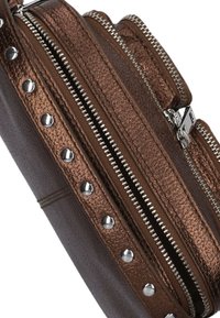 Bruine leren tas met een gestructureerde afwerking, zilverkleurige hardware, meerdere ritssluitingen en studaccenten langs de randen.
