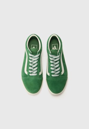 Paire de baskets en daim vert avec des bandes blanches sur les côtés et des lacets blancs, vues de dessus sur un fond blanc uni.