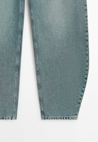 Lichtblauwe spijkerbroek met taps toelopende pijpen en zichtbare zijnaden, getoond vanaf halverwege de dij tot de enkel tegen een witte achtergrond.