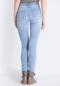 Los jeans ajustados de mezclilla en azul claro presentan una cintura alta y bolsillos traseros, combinados con botas de tobillo grises con flecos.