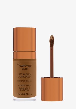 Brun concealer i en klar glasflaska med ett guld-orange metallock. Inkluderar en borsteapplikator med en texturerad spets.