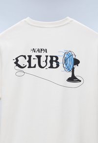 Λευκό πουκάμισο με το κείμενο "NAPA CLUB" και απεικόνιση ενός μαύρου επιτραπέζιου ανεμιστήρα που φυσά γαλάζιο αέρα στο πίσω μέρος.