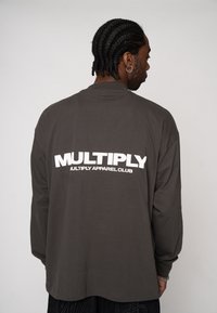 Long-sleeve, gray cotton t-shirt featuring bold white text "MULTIPLY" and "MULTIPLY APPAREL CLUB" on the back, relaxed fit.