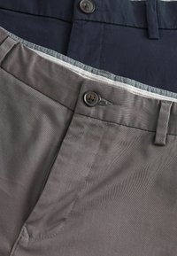 Kaksi paria housuja: yksi tummansininen ja yksi harmaa. Molemmissa on sileä puuvillakangas, nappikiinnitys ja hienovarainen kuvioitu vyötärönauha.