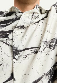 Kevyt kangas, jossa mustia abstrakteja kuvioita kermaisella pohjalla; napitettava paita, jossa klassinen kaulus ja läpinäkyvät napit.