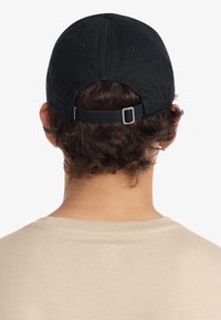 Gorra negra de algodón con visera curva y correa ajustable, con acabado texturizado y una etiqueta en el lateral. Usada al revés.