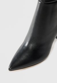 Black leather ankle boot with pointed toe and block heel on white background, showing smooth texture and clean design.