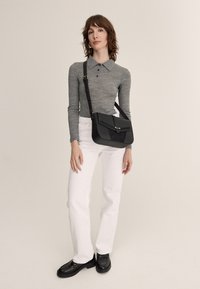 Black crossbody bag with smooth leather and suede accents, featuring a flap closure and a single metal button. Model wears light grey top and white jeans.