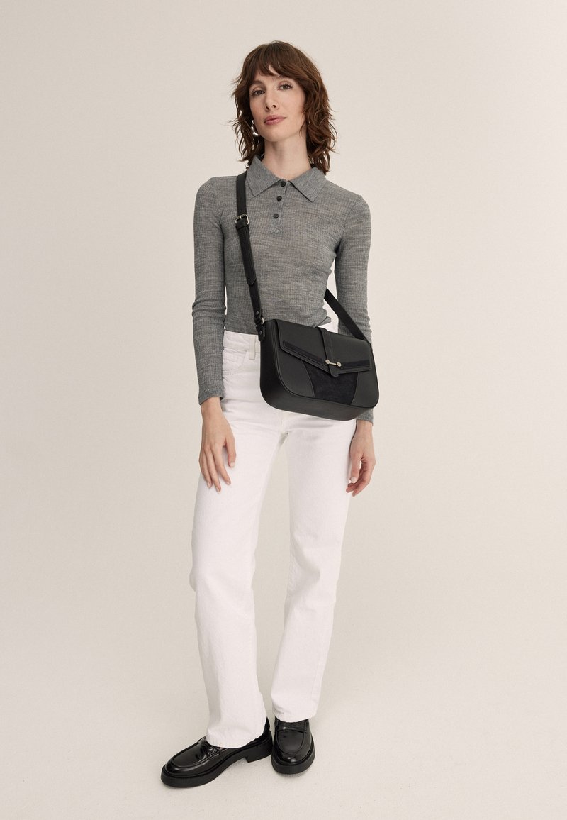 Black crossbody bag with smooth leather and suede accents, featuring a flap closure and a single metal button. Model wears light grey top and white jeans.