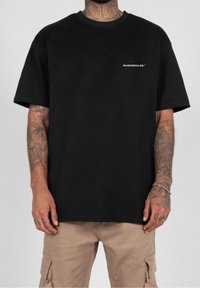 T-shirt in cotone nero con scollo rotondo e maniche corte. Presenta il logo bianco "MJGONZALES" sulla parte sinistra del petto. Design a vestibilità ampia.