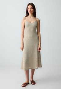 Beige gebreide slipdress met een chevronpatroon, spaghettibandjes en een uitlopende zoom, gecombineerd met bruine sandalen.