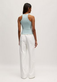 Lichtblauw, mouwloos tanktopje gecombineerd met witte, loszittende broeken. Het topje heeft een aansluitend ontwerp, terwijl de broek een elastische tailleband heeft.