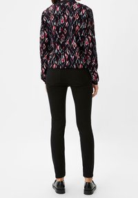 Pantalones negros de corte ajustado combinados con una blusa estampada que presenta detalles en rojo y blanco sobre un fondo negro. Textura suave, tejido elástico.