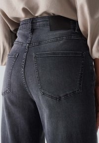 Vaqueros de talle alto en gris oscuro, con bolsillos traseros, una etiqueta de cuero en la pretina y una textura sutil.