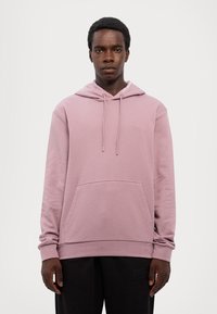 Világos rózsaszín kapucnis sweatshirt, puha anyagból készült, kenguruzsebbe, állítható húzózsinórokra és diszkrét logó részletre a nyaknál.