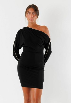 Abito nero off-the-shoulder realizzato in tessuto lucido, con maniche lunghe e dettagli con zip, silhouette aderente e lunghezza a metà coscia.