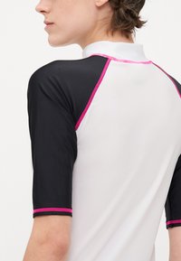 Kortärmad rash guard, med en vit kropp och svarta ärmar samt rosa detaljer. Materialet verkar vara slätt, med en sportig, figurnära design.