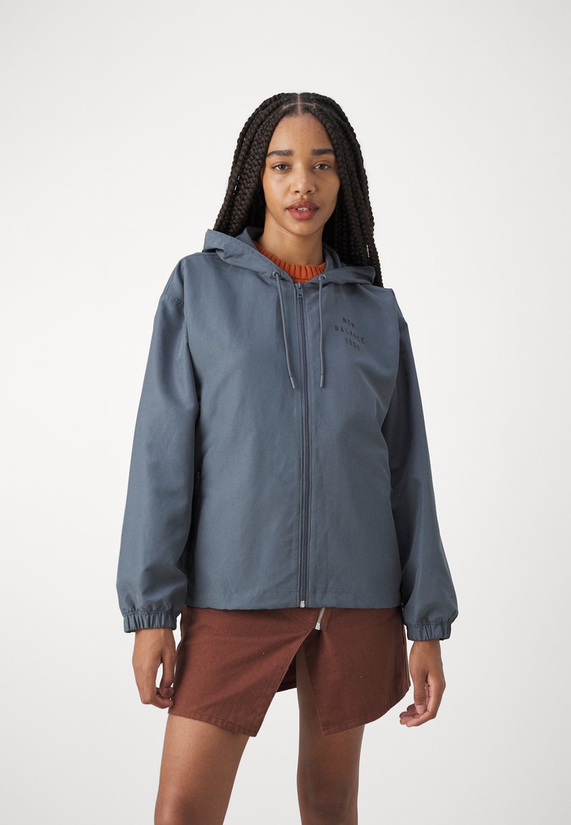 Kapuzensweatjacke aus dunkelblauem Stoff mit lockerer Passform. Verfügt über elastische Bündchen und den Aufdruck "NEW BALANCE 1986" auf der Brust.