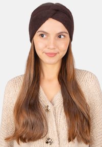 Bandeau en tricot brun avec un design torsadé, présentant une texture douce. Porte avec un cardigan en tricot beige, mettant en valeur des boutons.