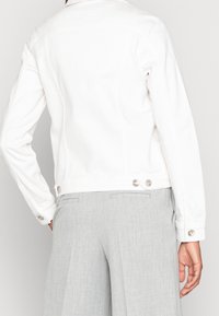 Biała dżinsowa kurtka z kołnierzem, długimi rękawami, srebrnymi guzikami na mankietach oraz dopasowanym krojem o gładkiej fakturze.