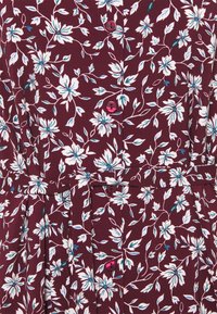 Burgundy klänning med vit och teal blommönster, med rosa knappar, plisserad midja och korta ärmar. Mjuk tygstruktur.