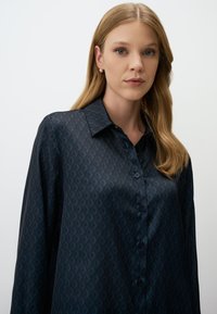 Long-sleeve shirt in dark blue satin featuring a diamond pattern, structured collar, and button closure down the front.
