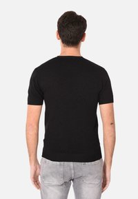 Maglione nero a maniche corte in maglia con scollatura a girocollo. Il tessuto sembra morbido e ha una consistenza liscia. Indossato con jeans grigi chiari, che mostrano una silhouette aderente.