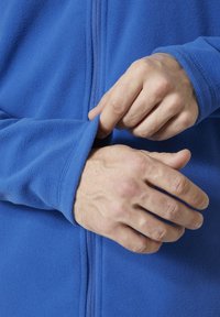 Blauwe fleece jack met een volledige rits; handen die de mouw aanpassen; zachte textuur en gestroomlijnd ontwerp.