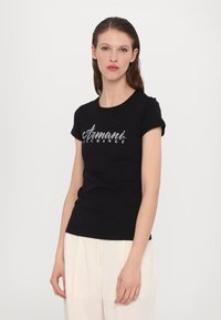 Zwarte katoenen T-shirt met korte mouwen met een glinsterend zilveren "Armani Exchange" logo over de borst. Strakke pasvorm, ronde halslijn.