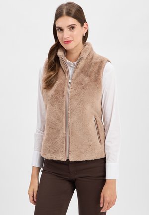 Tan nepbontvest met hoge kraag, voorrits en zijzakken, gedragen over een witte blouse. Gladde textuur, casual ontwerp.