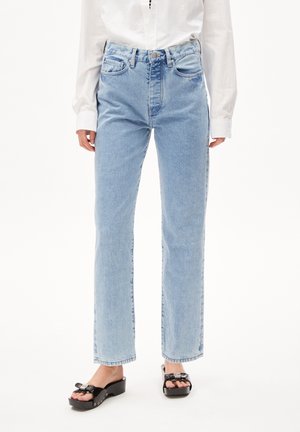 Person trägt hellblaue Jeans mit geradem Bein, weißes langärmliges Hemd und schwarze Plateau-Sandalen mit Schnallendetails.