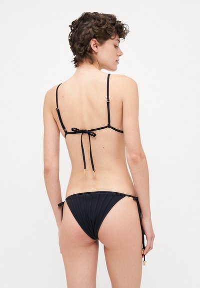 Melna bikini komplekts ar aizsietu aizmuguri ar plāniem siksniņām, zeltainiem aksesuāriem un teksturētu audumu apakšā ar regulējamiem sānu saitēm.