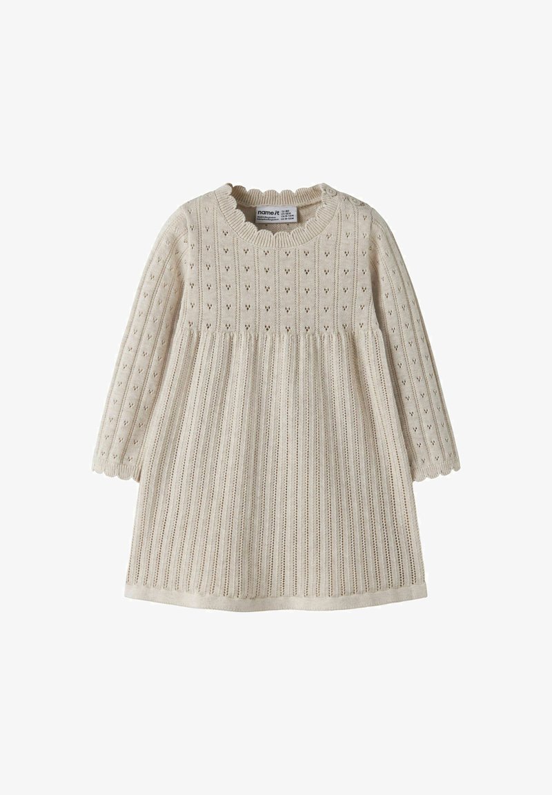 Robe de bébé tricotée couleur crème avec manches longues, bords festonnés et petits motifs ajourés sur la partie supérieure et les manches.