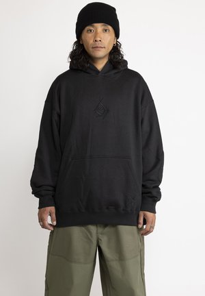 Black hoodie with a front pocket, featuring embroidered designs. Made of soft fabric, it has a relaxed fit and ribbed cuffs. Paired with olive green pants.