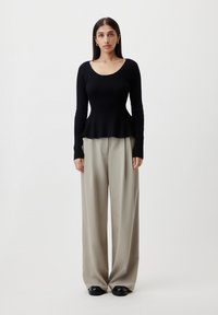 Black ribbed long-sleeve top with a scoop neckline, paired with wide-leg beige trousers and black shoes; minimalistic and tailored design.