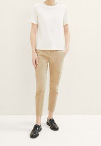 White short-sleeve t-shirt, beige fitted pants with front pockets and stitching details, black lace-up shoes. Simple, streamlined design.