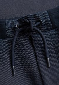 Pantaloni da allenamento navy con tessuto testurizzato, vita elastica e cordino a contrasto con punte metalliche per la regolazione.