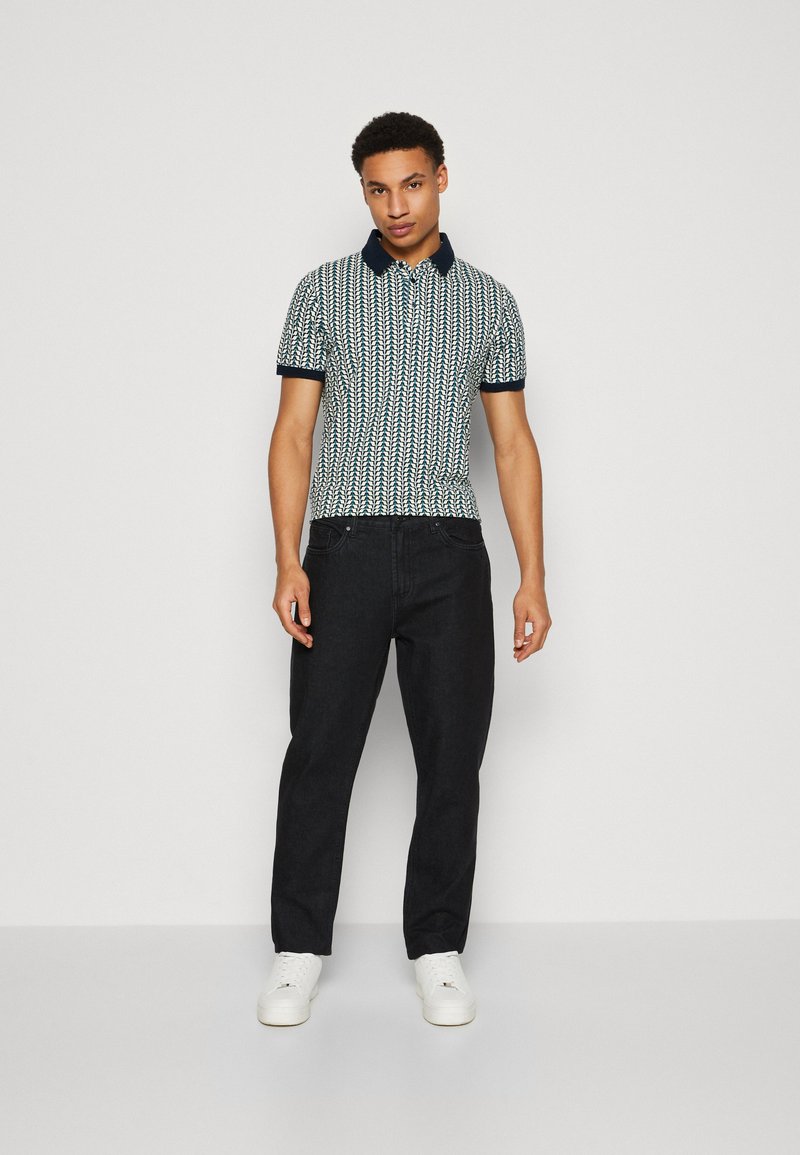 Kurzarm-Polohemd im Navy-und-Weißen Muster mit einem kontrastierenden Marinekragen. Kombiniert mit dunklen Jeans und weißen Sneakers.