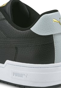 Gros plan sur le talon d'une basket Puma noir et blanc avec cuir texturé, logo Puma doré et semelle en caoutchouc blanche embossée du logo Puma.