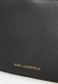 Black leather product featuring a textured surface with a gold logo reading "KARL LAGERFELD" prominently displayed.